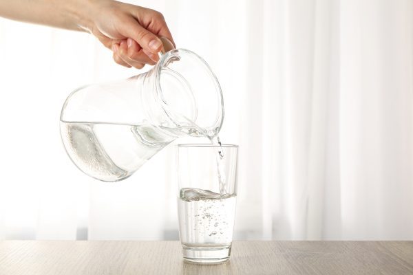 pouring-purified-fresh-water-from-jug-glass-wooden-table