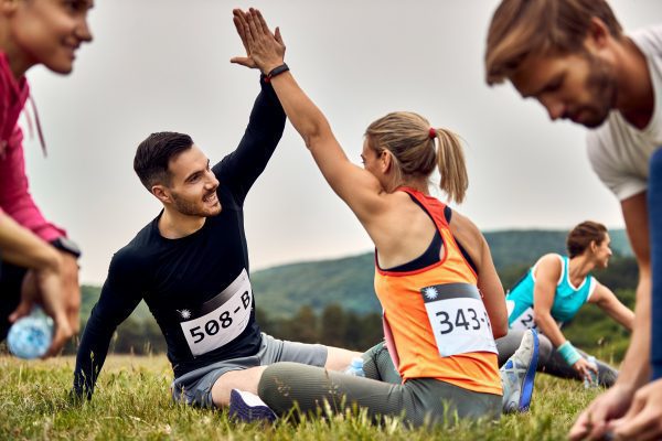 young-happy-couple-giving-highfive-each-other-while-stretching-grass-before-marathon-race