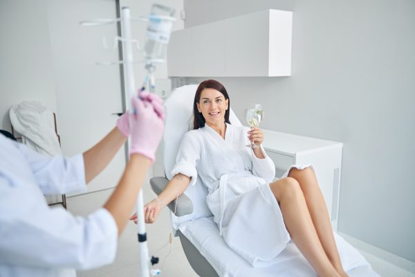 smiling-pleased-female-patient-with-glass-healthy-drink-sitting-cosmetic-chair