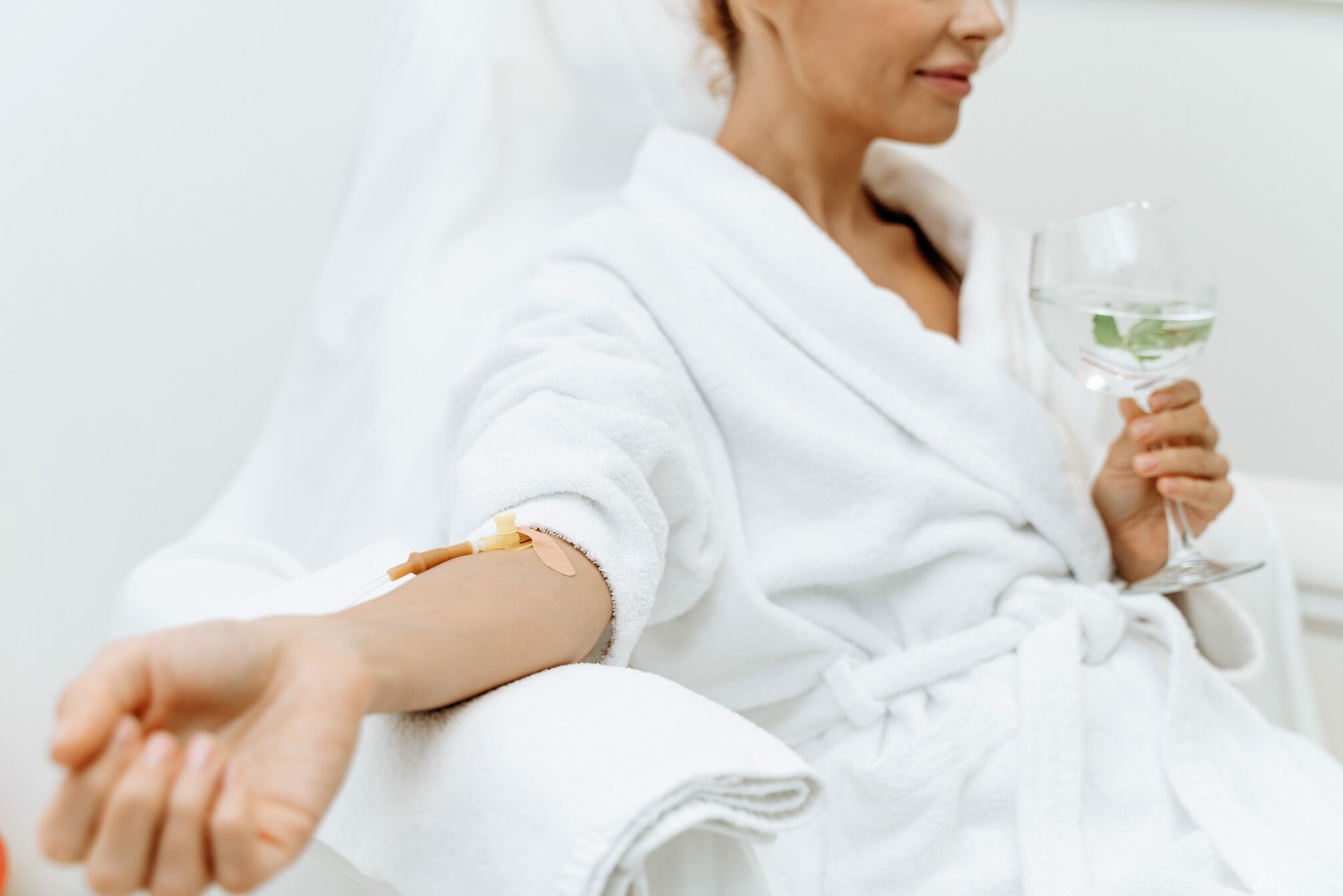 close up calm female patient sitting with tube needle during iv infusion girl holding glass with lemon water relaxing 1